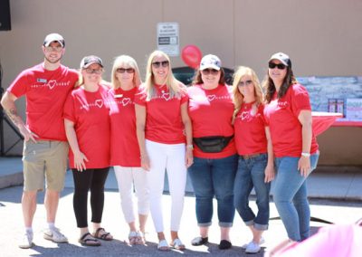 A group of six women and a man smiling at the camera and wearing red shirts that say "Associa Cares"