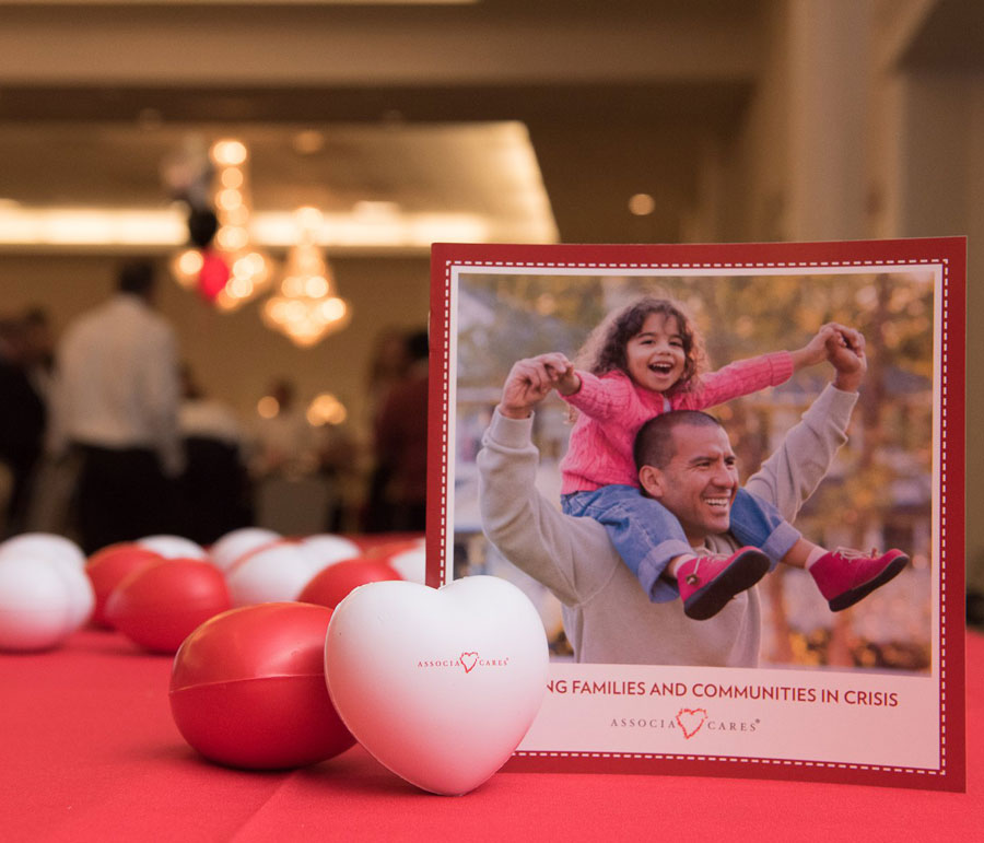 An image of a card on a table with a picture of a man with his daughter on his shoulders. The card says Helping Families and Communities in Crisis. Associa Cares.