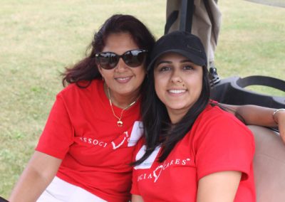 Two women wearing red Associa Cares shirts smile from a golf cart