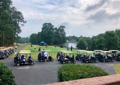 A line of 20 or so golf carts in front of a green.