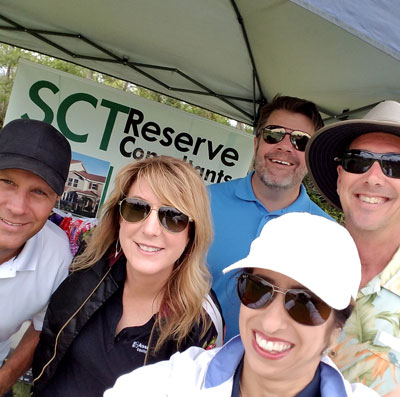 A group of 2 women and 3 men smiling in front of an event tent with a sign that says SCT Reserve Consultants